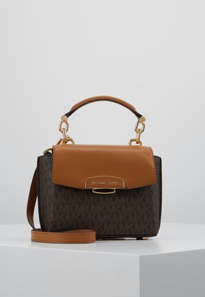 Kleine Michael Kors handtas met bruine leren klep en handvat, donker lichaam met logopatroon en verstelbare schouderriem op een witte ondergrond.