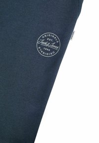 Donker marineblauwe sweatshirt met een rond logo in lichtgrijs, inclusief tekst en oprichtingsdatum. Gladde textuur en casual ontwerp.