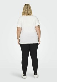 Hvid kortærmet top med dekorative syninger på ærmerne, parret med sorte leggings og hvide sneakers. Glat stofstruktur.