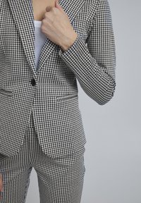 Musta-valkoinen koiranhampaiden kuviollinen bleiseri, jossa yksi nappi, räätälöity istuvuus ja hienovarainen tekstuuri kangas; puettuna valkoisen topin päälle.