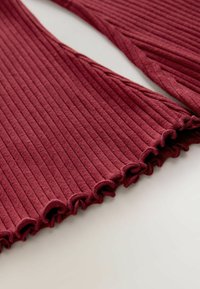 Ribbet bordeaux stof med bølgede kanter, der har en blød tekstur og vandrette linjer. Designet fremhæver en tætsiddende silhuet.