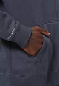 Sudadera de color azul oscuro con bolsillo tipo canguro y puños acanalados, hecha de una tela suave con un detalle del logo "Storm1" en la manga.