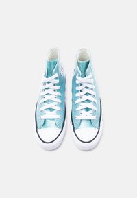 Ζευγάρι τουρκουάζ ψηλά αθλητικά παπούτσια με λευκά κορδόνια και λαστιχένιες μύτες, σε θέα από πάνω πάνω σε ανοιχτό φόντο.