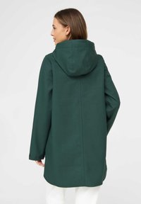 Chaqueta verde con capucha y acabado texturizado, con corte recto, bolsillos laterales y puños abotonados. Tejido suave, líneas limpias.