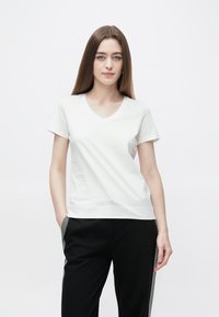 Λευκό βαμβακερό μπλουζάκι με V λαιμόκοψη, κοντά μανίκια και άνετη εφαρμογή, συνδυασμένο με μαύρο παντελόνι που έχει λωρίδες στο πλάι.