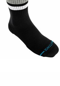 Calcetín negro con textura acanalada, que presenta una franja blanca en la parte superior y un detalle de logo azul en la puntera. Diseño de longitud hasta el tobillo.