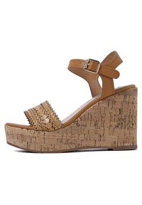 Sandalo a zeppa in pelle marrone con una fascia intrecciata e suola intermedia in sughero. Presenta una cintura regolabile alla caviglia e una superficie in sughero texturizzata.