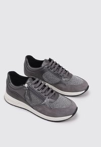 Sneaker grigie che presentano un mix di materiali lisci e testurizzati, allacciatura frontale, zip decorativa e suola in gomma bianca.