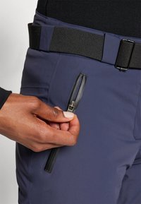Sötétkék kültéri nadrág vízszintes cipzáros zsebbel, karcsú dizájnnal és állítható fekete övvel a derekán. Textúrált szövetfelület.
