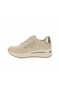 Zapatilla deportiva beige claro con panel lateral perforado, diseño con cordones, suela blanca gruesa y detalle metálico dorado en el talón.