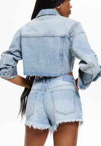 Veste en denim bleu clair coupée avec un ourlet effiloché, assortie à un short taille haute avec des bords effilochés et des poches arrière.