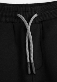 Czarne dresy z materiału z prążkowanym pasem w talii oraz szarym sznurkiem do ściągania o warkoczowej strukturze z plastikowymi końcówkami.