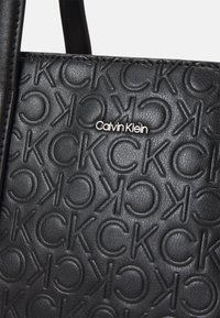 Mustassa tekonahkaisessa olkalaukussa on kohokuvioitu logo-kuviointi ja hopeinen Calvin Klein -kilpi. Laukussa on sileä pinta ja kestävät kantokahvat.