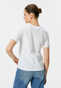 Camiseta blanca de manga corta con cuello redondo. Tela de algodón suave y liscia. Combinada con unos vaqueros de tiro alto azules, que muestran un ajuste relajado.