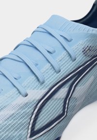 Svetlomodri športni čevelj z usklajenimi vezalkami, zgornji del iz teksturirane tkanine in temnomodrim geometrijskim vzorcem blizu podplata.