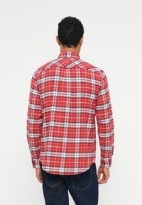 Camicia a quadri rossi con un motivo di linee bianche e blu, maniche lunghe, polsini con bottone e orlo diritto con spacco laterale.