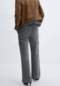 Pantalons cargo gris avec une coupe large, dotés de plusieurs poches et d'une texture durable, associés à une veste en daim marron.