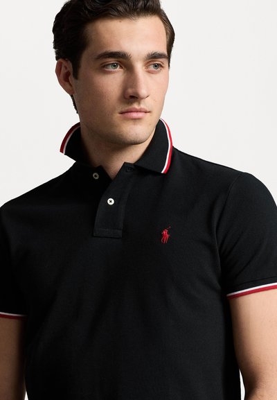 Black polo shirt with a red embroidered logo, featuring a striped red and white collar. Made of textured fabric and designed with a two-button placket.
