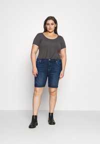 Szürke, rövid ujjú póló, kék farmer bermuda rövidnadrág elülső zsebekkel és fekete bokacsizmával. Simák anyag és testhezálló dizájn.