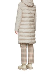 Beige gewatteerde jas met een capuchon, contrasterende gestructureerde mouwen en een rechte snit, gecombineerd met een geruit broek en beige enkellaarsjes.