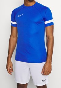 Blue athletic t-shirt with white stripes on sleeves, made of smooth fabric. Paired with white shorts, featuring a small Nike logo.