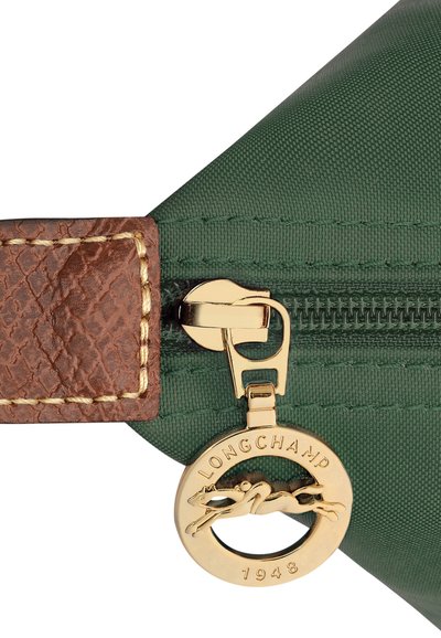 Grüne Stofftasche mit einem strukturierten braunen Lederriemen, ausgestattet mit einem goldenen Reißverschluss und einem runden goldenen Anhänger mit Pferdemotiv und Markenkennzeichnung.