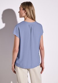 Blusa azzurro chiaro a maniche corte con dettaglio di piega sul retro, texture liscia, orlo arrotondato e design senza decorazioni.