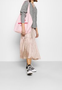 Grauer Strickpullover, pinke Blum Midi-Rock, schwarz-weiße Sneaker. Pinke Tragetasche mit roten Schriftzügen, Schulterriemen, lässiger Look.
