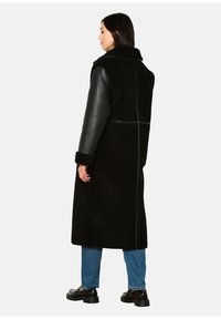 Zwarte jas met een fuzzy, textuur lichaam en gladde leren mouwen. Lange stijl met een rechte snit, afgewerkt met een opgestroopte kraag.