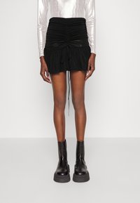 Schwarzer Minirock mit geraffter Textur, Kordelzugdetails und ausgestelltem Saum. Kombiniert mit klobigen schwarzen Leder-Stiefeletten. Glatt und mehrlagig.
