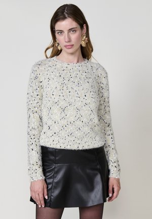 Weißer strukturierter Pullover mit schwarzen und goldenen Sprenkeln, runder Ausschnitt, lange Arme, kombiniert mit einem schwarzen Lederminirock.