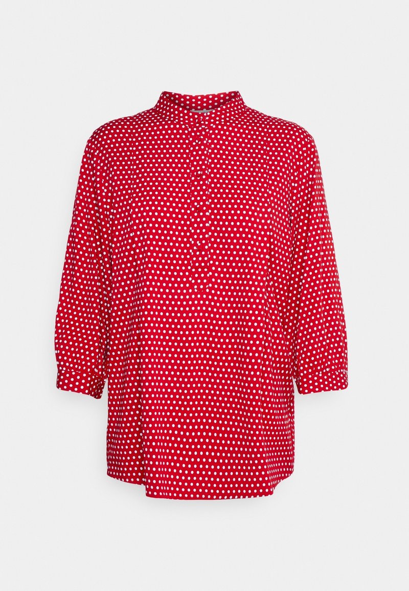 Blouse rouge à pois blancs, manches trois-quarts, patte de boutonnage sur le devant et col montant court.