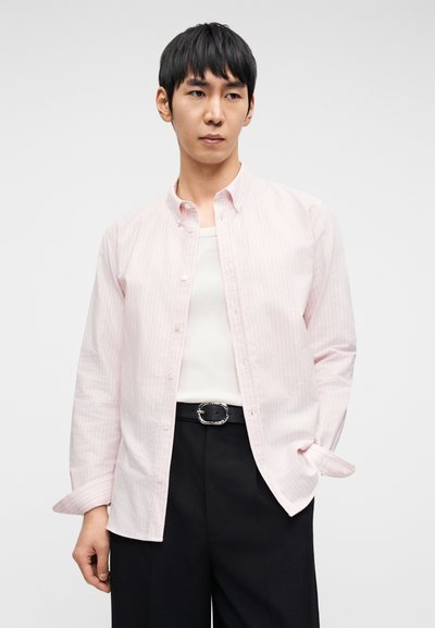 Ροζ ανοιχτό ροζ πουκάμισο με κάθετες λευκές ρίγες, μακριά μανίκια και απαλή υφή, συνδυασμένο με λευκό αμάνικο τοπ και μαύρο παντελόνι.