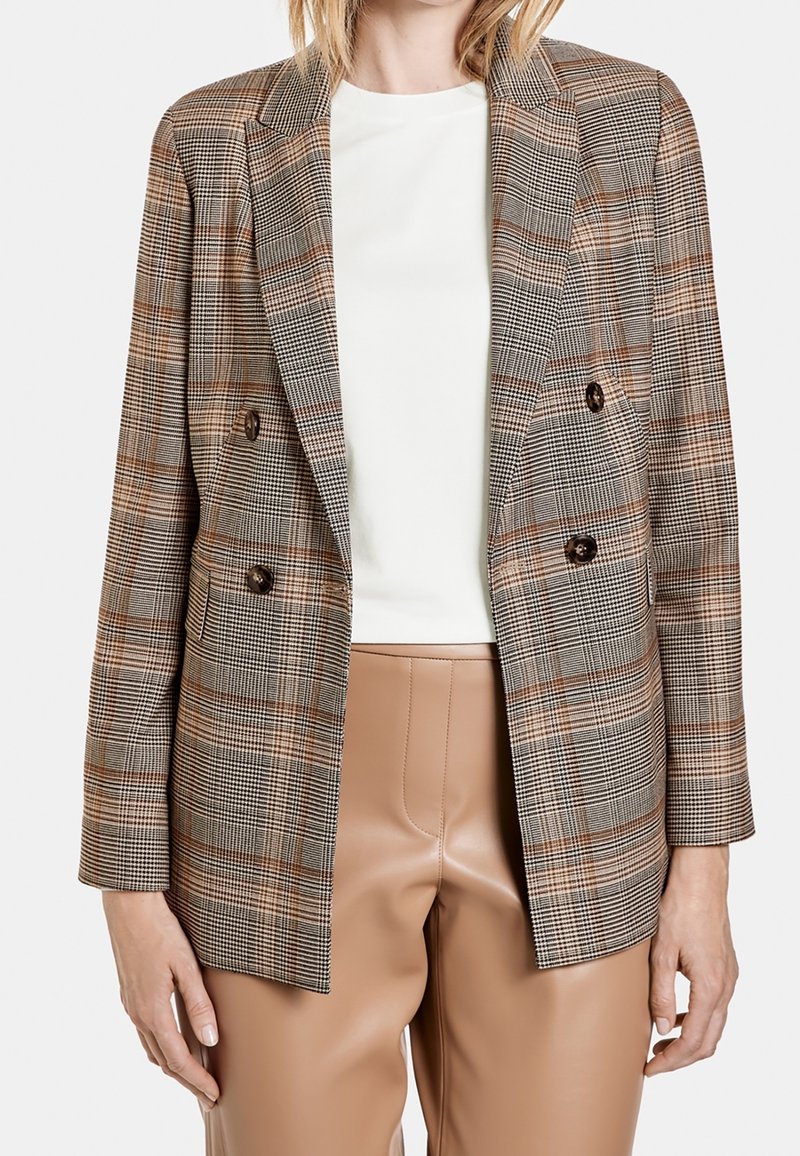 Blazer croisé à carreaux marron, avec des boutons marron, une coupe ajustée et des épaules structurées. Associé à un pantalon en simili cuir marron clair.
