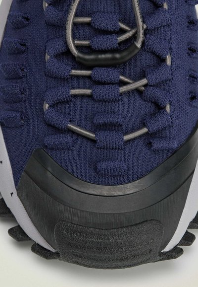 Sneaker in tessuto blu navy con parte superiore texturizzata, lacci elastici grigi e suola in gomma nera rinforzata con scanalature per la trazione.