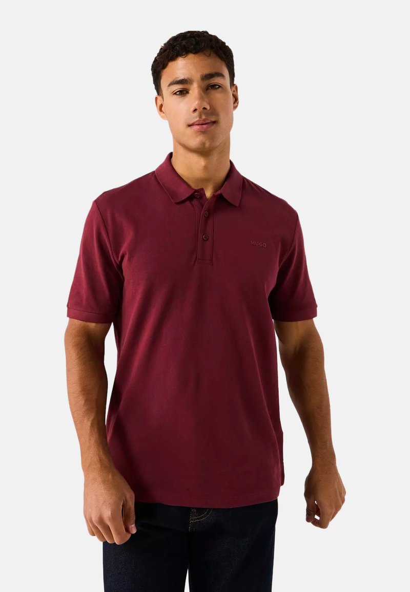 Polo en color burdeos hecho de algodón, con cuello, mangas cortas y un logo sutil en el pecho. Textura suave, diseño informal.