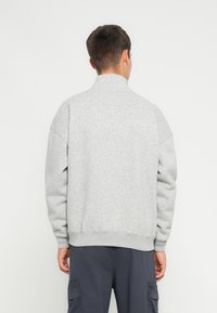 Sudadera gris con cuello alto, corte holgado y puños acanalados. La tela parece suave con una textura lisa y un diseño minimalista.