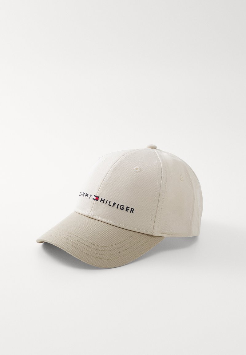 Gorra de béisbol beige hecha de una mezcla de algodón, con un visor curvado y el logotipo bordado "TOMMY HILFIGER" en negro. Diseño clásico de seis paneles.