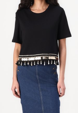 Czarny top z krótkim rękawem z teksturowanym brzegiem zdobionym metalicznymi dyskami i frędzlami. Do tego spódnica dżinsowa z guzikami.