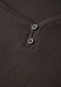 Tissu tricoté marron avec un décolleté en V, comportant deux boutons gris et des détails de couture visibles. Texture lisse avec un design ajusté.
