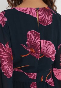 Bloemenjurk met een marineblauwe achtergrond en grote roze bloemen. Knopen aan de achterkant met een split, vloeiend materiaal en een zachte textuur.