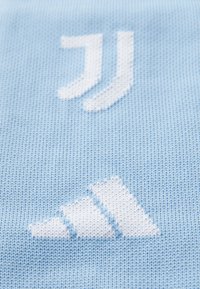 Svetle modrá pletená látka se bílými logy, včetně stylizovaných písmen a geometrického tvaru, s hladkým povrchem.