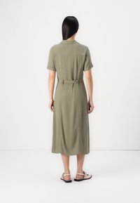 Robe midi vert olive à manches courtes, avec une taille ceinturée et une coupe décontractée. Texture lisse et détails subtils sur l'empiècement du dos.