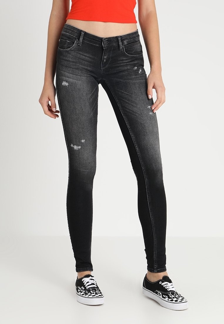 Pantalones vaqueros ajustados negros con un lavado descolorido, detalles rasgados y un ajuste slim. Combinados con zapatillas de deporte en blanco y negro con un patrón.