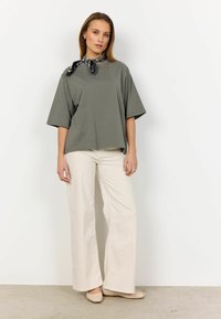 Grå overdimensioneret T-shirt med korte ærmer, parret med lyse beige vide bukser. Sort og hvid mønstret tørklæde om halsen.