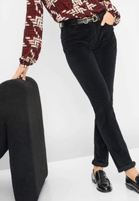 Zwarte corduroy broeken met een slim fit, voorzien van een glanzende zwarte riem met gouden hardware, gecombineerd met een gebloemde blouse. Zwarte instappers maken de look compleet.