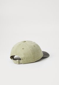 Groene katoenen pet met een donkergrijze klep. Heeft een verstelbare band aan de achterkant en gestikte details. Zachte textuur met ventilatiegaten.