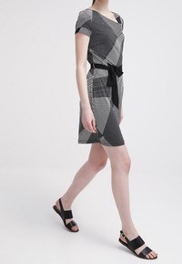 Svartvitt mönstrad klänning med korta ärmar och midja med bälte. Bärs med svarta platta sandaler som visar geometriska och randiga mönster.