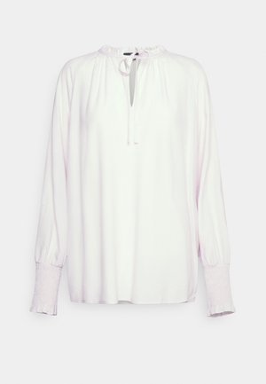 Blusa rosa clara feita de tecido suave, com um decote franzido, uma abertura em forma de gota e punhos franzidos com uma borda ondulada.