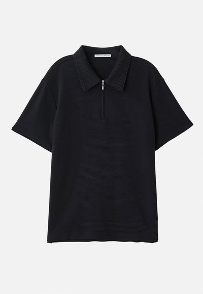 Mustmustärk musta polo särk, millel on poolkattega krae, valmistatud soonikust riidest. Lühikesed varrukad ja pehme istuvus. Ilma nähtavate mustrite või aktsentideta.